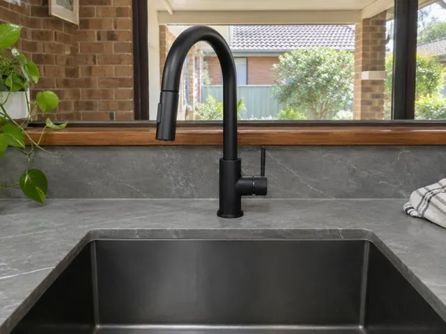 Black kitchen mixer tap over a stainless sink with stone benchtop and tiled splashback in Metford